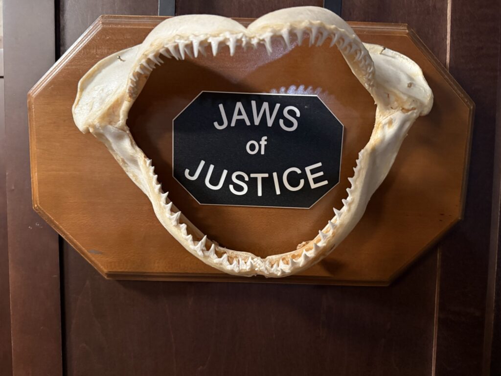 picture of a plaque: a large skeletal mouth with many teeth is affixed to the plaque; a sign reading "Jaws of Justice" centered on plaque.